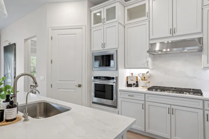 Kitchen featuring white cabinetry, quartz countertops with a full-height stone backsplash, stainless steel built-in double ovens, a gas cooktop, and a stainless steel kitchen faucet