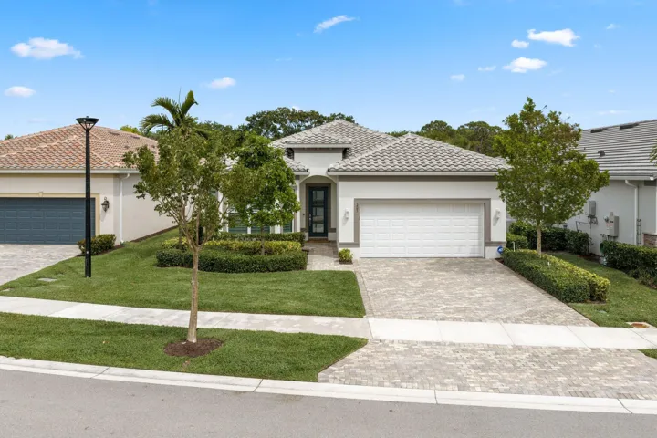 Stucco exterior featuring a tiled roof, paver driveway, two-car garage, and manicured landscaping