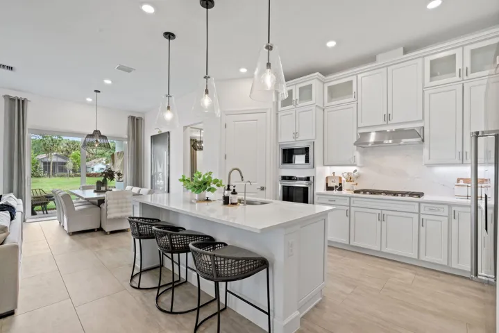 Kitchen featuring white shaker-style cabinetry, a large central island with quartz countertops, stainless steel built-in double wall ovens, a gas cooktop with a stainless steel range hood, and porcelain tile flooring