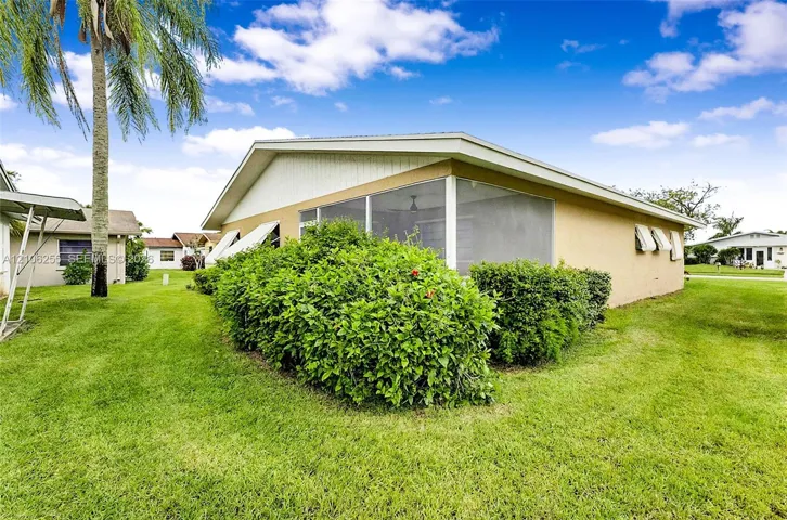 Stucco exterior residence featuring a screened-in lanai, decorative window awnings, and landscaped perimeter shrubbery set on a level lawn