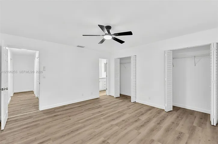 Room featuring wood-finish flooring, a matte black ceiling fan with an integrated light fixture, and dual closets with bi-fold doors