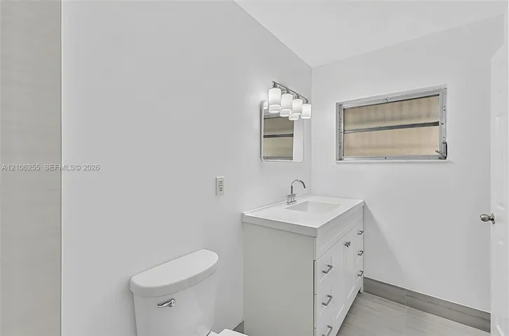 White vanity with integrated basin, multi-drawer storage, polished metal faucet, multi-bulb vanity light, and gray tile flooring