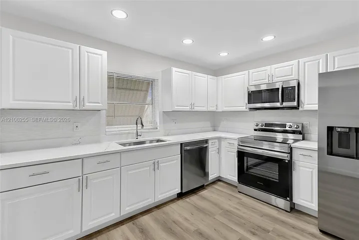 Kitchen featuring white shaker-style cabinetry, quartz countertops, stainless steel appliances, recessed lighting, and wood-finish flooring