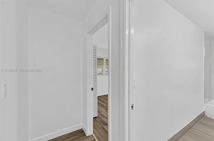 Interior space featuring wood-finish flooring, white walls, louvered closet doors, and tile flooring