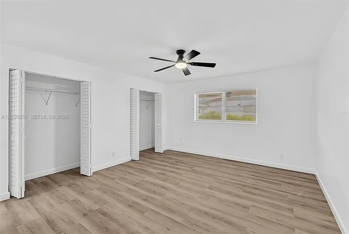 Neutral-toned wood-finish flooring, two closets with louvered folding doors, and a ceiling-mounted light fixture with fan
