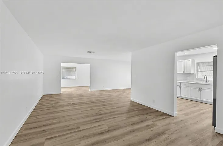 Open interior space featuring wood-finish flooring, white walls, and a kitchen area with white cabinetry and a stainless steel faucet