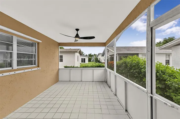 Screen-enclosed porch featuring white tile flooring, stucco wall finish, and a ceiling-mounted matte black fan