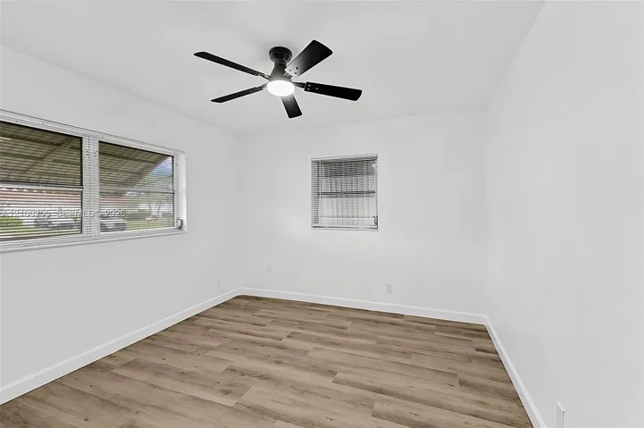 Room featuring wood-finish flooring, white walls, and a multi-blade ceiling fan with integrated lighting