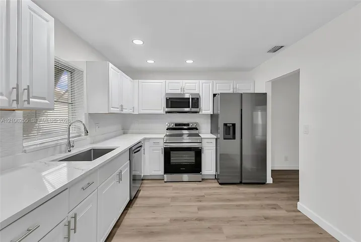 Kitchen featuring white shaker-style cabinetry, white quartz countertops, stainless steel appliances, and wood-finish flooring