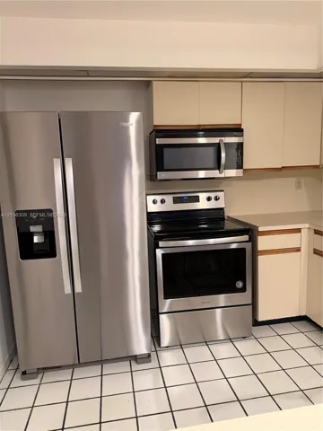 Stainless steel side-by-side refrigerator, stainless steel electric range, built-in microwave, light-toned cabinetry, and tiled flooring