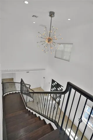 Staircase featuring dark wood-finish treads and a decorative metal railing, highlighted by a multi-point sputnik-style chandelier, recessed lighting, and high-ceiling architecture