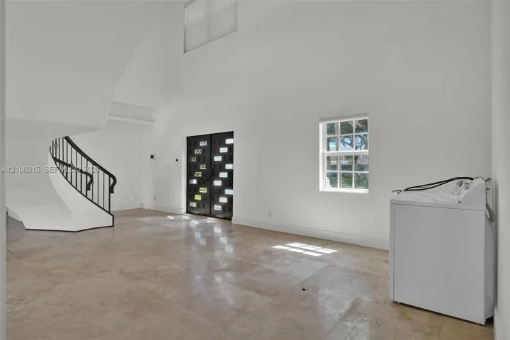Double-height foyer featuring stone tile flooring, a curved staircase with a metal handrail, and a decorative double entry door with glass paneling