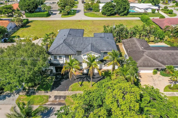 Two-story residence featuring a dark-toned tile roof, exterior white cladding, multiple mature palm trees, and a paved driveway