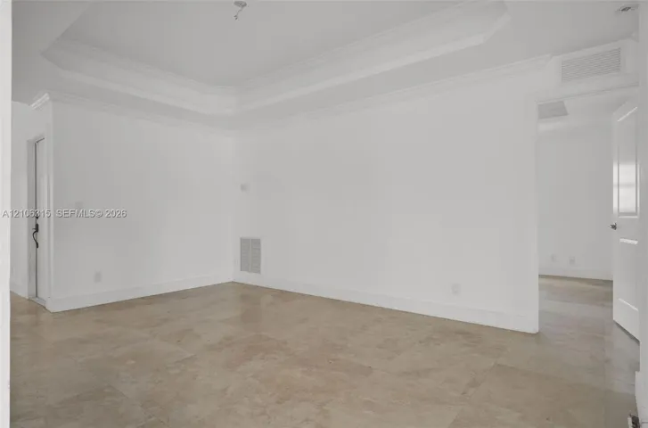 Interior space featuring a recessed tray ceiling, crown molding, and large-format neutral tile flooring