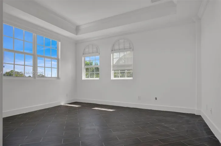 Room featuring dark tile flooring, a tray ceiling, and windows with arched upper panes