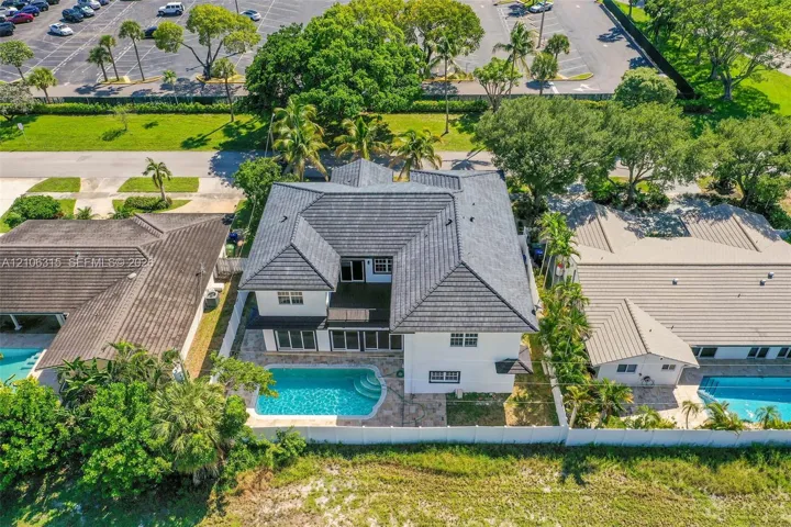 Two-story residence featuring a dark-toned tile roof, exterior stucco finish, private swimming pool, and stone-paver pool deck enclosed by white perimeter fencing