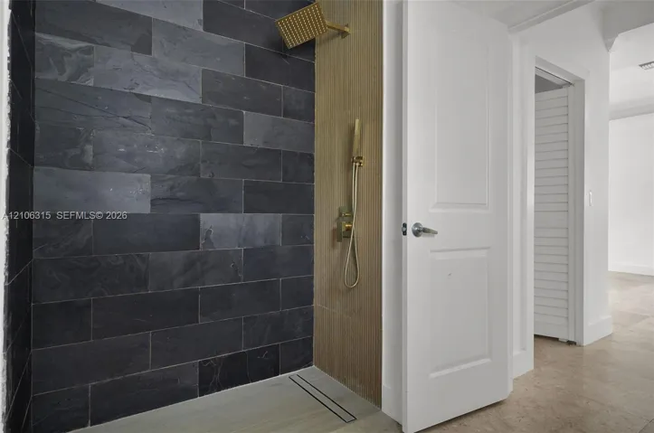 Walk-in shower featuring charcoal-toned stone tile, vertical wood-finish paneling, brushed metallic rainfall shower head with handheld sprayer, and a linear floor drain