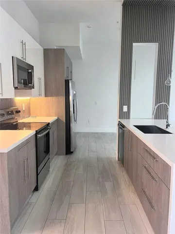 Kitchen featuring flat-panel cabinetry with wood-finish and high-gloss white upper doors, stone-finish countertops, stainless steel appliances, and vertical slat wall detailing