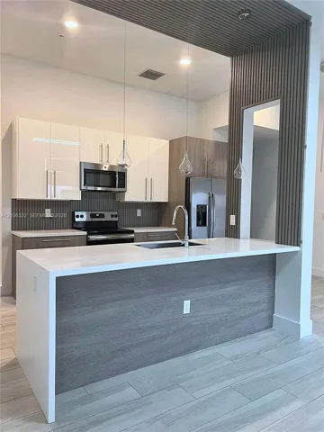Kitchen featuring a central island with a waterfall-edge quartz countertop, two-tone flat-panel cabinetry, vertical wood-slat accent wall, stainless steel appliances, and wood-finish tile flooring
