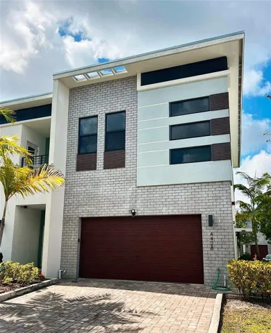 Modern two-story architectural exterior featuring a combination of light-toned brick masonry, horizontal panel siding, a single-car garage with wood-finish door, clerestory windows, and a paved driveway