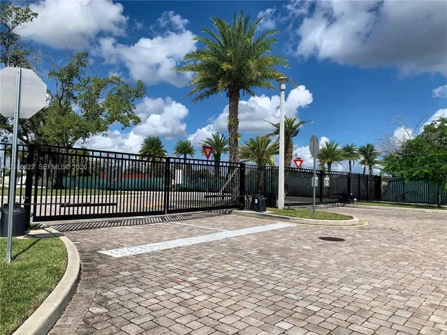 Gated entry featuring black iron fencing, paver driveway, and mature palm trees