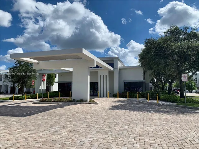 Modern architectural facade with a prominent cantilevered porte-cochère, paver driveway, vertical accent detailing, and perimeter bollard lighting