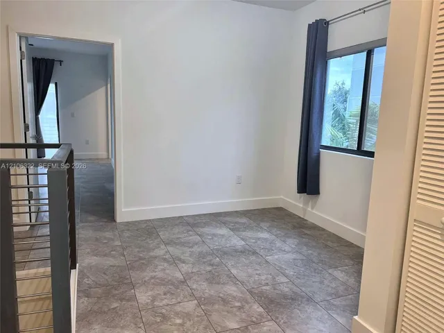 Neutral-toned tile flooring, metal horizontal-bar railing, and white interior walls featuring a window with a black frame