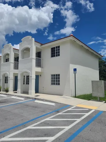 Stucco exterior with multi-level covered balconies, grid-pane windows, and a paved parking area