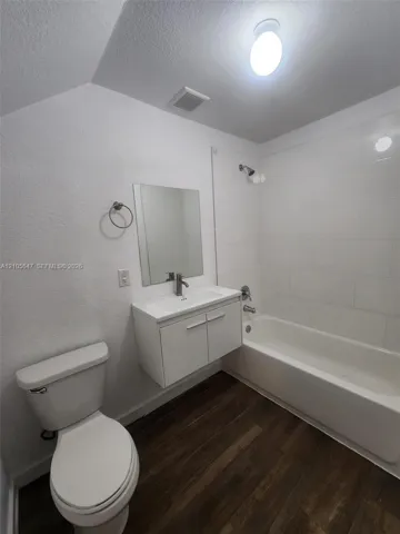 Bathroom featuring a floating vanity with a white rectangular sink, white subway tile shower surround, chrome faucet, and wood-finish flooring