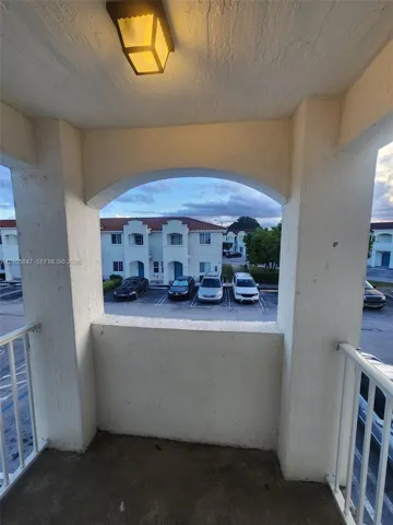 Covered balcony featuring a white metal railing, stucco walls, an arched opening, and a flush-mount exterior light fixture