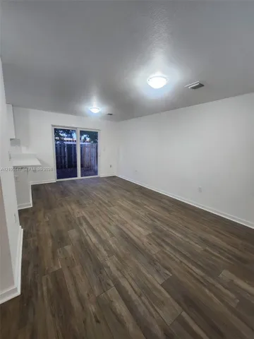 Wood-finish flooring, white walls, flush-mount ceiling lighting, and glass sliding door access to exterior grounds