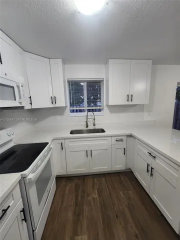 Kitchen featuring white shaker-style cabinetry, solid-surface countertops, wood-finish flooring, undermount stainless steel sink, and a pull-down faucet