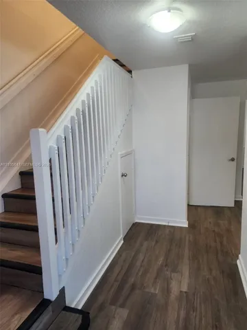 Staircase featuring wood-finish treads, white railing, and an integrated under-stair storage cabinet, complemented by wood-finish flooring and a flush-mount ceiling light fixture