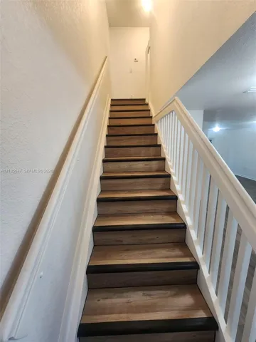 Staircase featuring wood-finish treads, dark-toned bullnose edges, white vertical balusters, and a matching white handrail