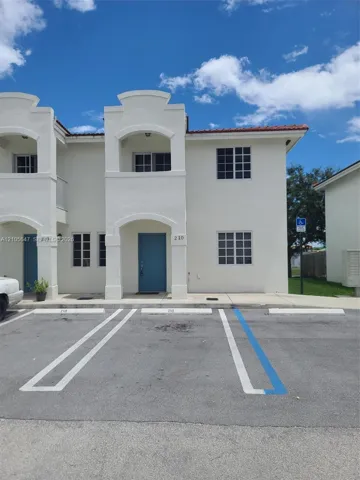 Two-story stucco exterior featuring arched entryway detailing, a covered second-story balcony, multi-pane windows, and dedicated asphalt parking