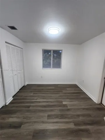 Wood-finish flooring, white louvered closet doors, and a central ceiling-mounted light fixture