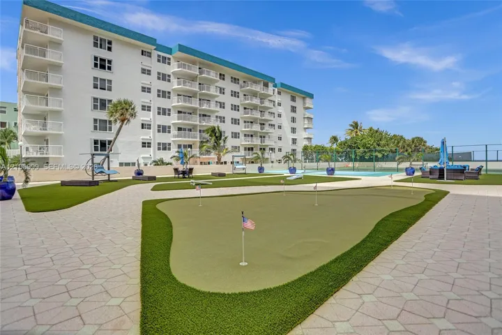 Multi-story residential building exterior featuring private balconies, a putting green, paved walkways, and tennis court access