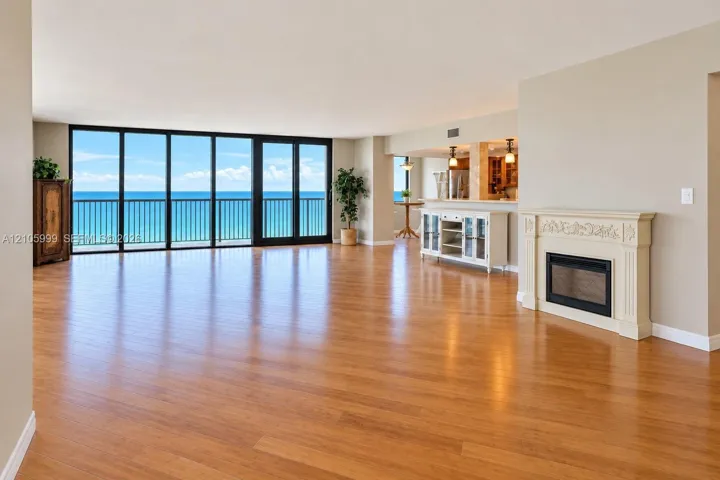 Open-concept living space featuring wood-finish flooring, floor-to-ceiling glass wall, decorative fireplace mantel, and ocean backdrop