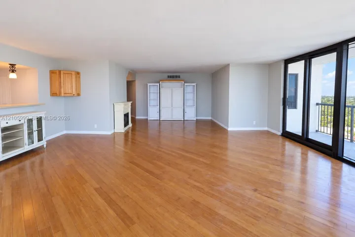Expansive living space featuring wood-finish flooring, a built-in mantle, floor-to-ceiling glass wall, and integrated cabinetry