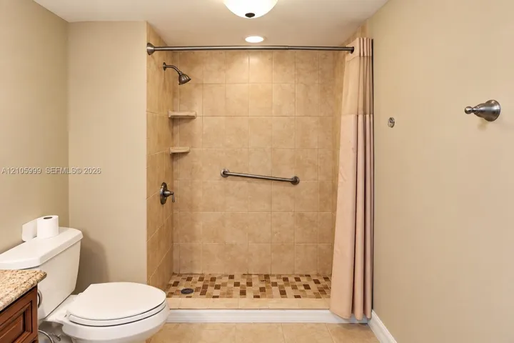 Walk-in shower with tile surround, mosaic tile flooring, built-in shelving, brushed nickel hardware, and a grab bar