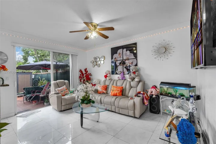 Large-format tile flooring, crown molding, ceiling fan with integrated lighting, and sliding glass doors providing outdoor access