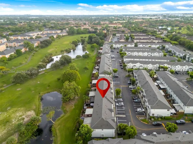 Aerial perspective of multi-story townhome community featuring asphalt shingle roofing, paved surface parking, and exterior green space