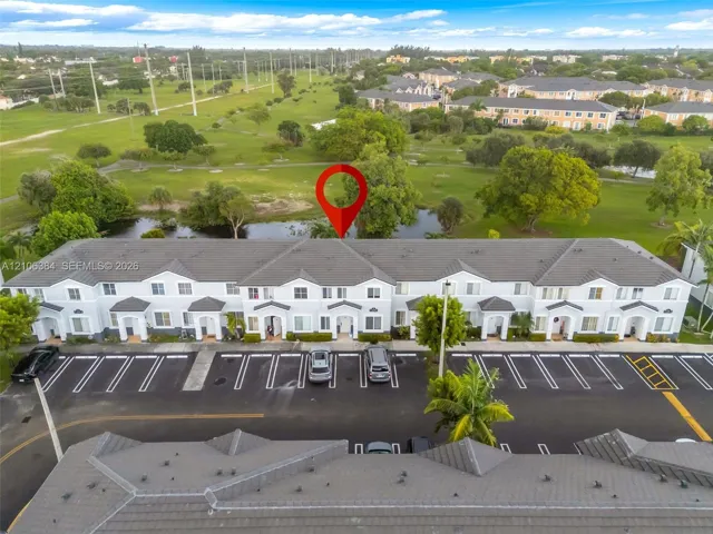 Multi-unit residential complex featuring a concrete tile roof, light-toned stucco exterior, dedicated surface parking, and perimeter pond frontage