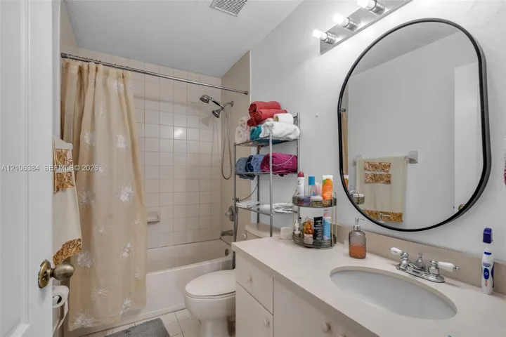 Bathroom featuring a vanity with integrated sink, oval wall-mounted mirror, three-light fixture, and a tiled shower-tub combination