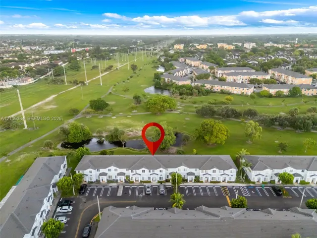 Aerial perspective featuring multi-story residential buildings, paved surface parking, a pond, and expansive green space