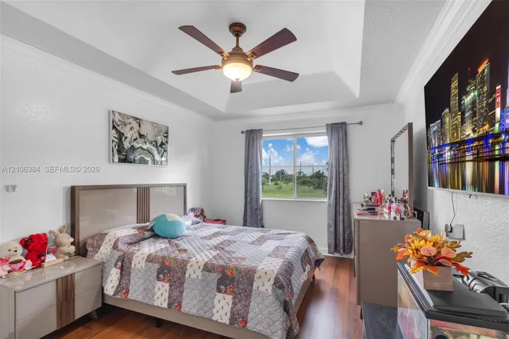 Tray ceiling, central ceiling fan with integrated lighting, and wood-finish flooring