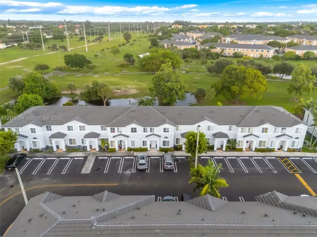 Multi-unit building exterior featuring a hip roof, stucco facade, covered entryways, and surface parking