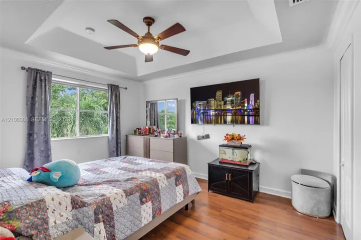 Tray ceiling featuring a center-mounted ceiling fan with light fixture, wood-finish flooring, and crown molding