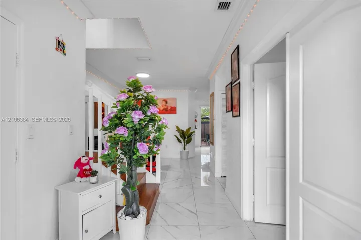 Interior hallway featuring white tile flooring with veining detail, recessed lighting, crown molding, and a staircase with wood treads and white balusters