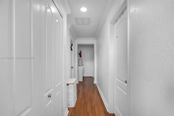 Hallway featuring wood-finish flooring, white arched-panel doors, and crown molding